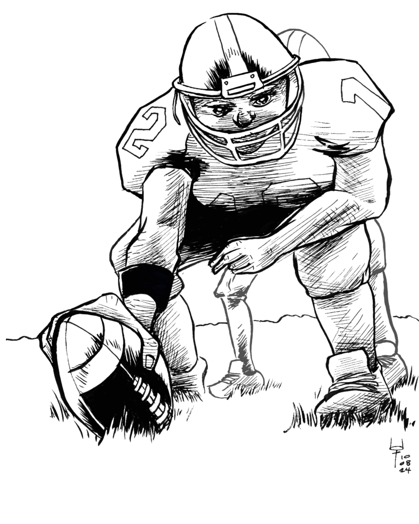 A football player is hunched over, holding a football to the grass in front of him. Behind him, the legs of the quarterback can be seen.